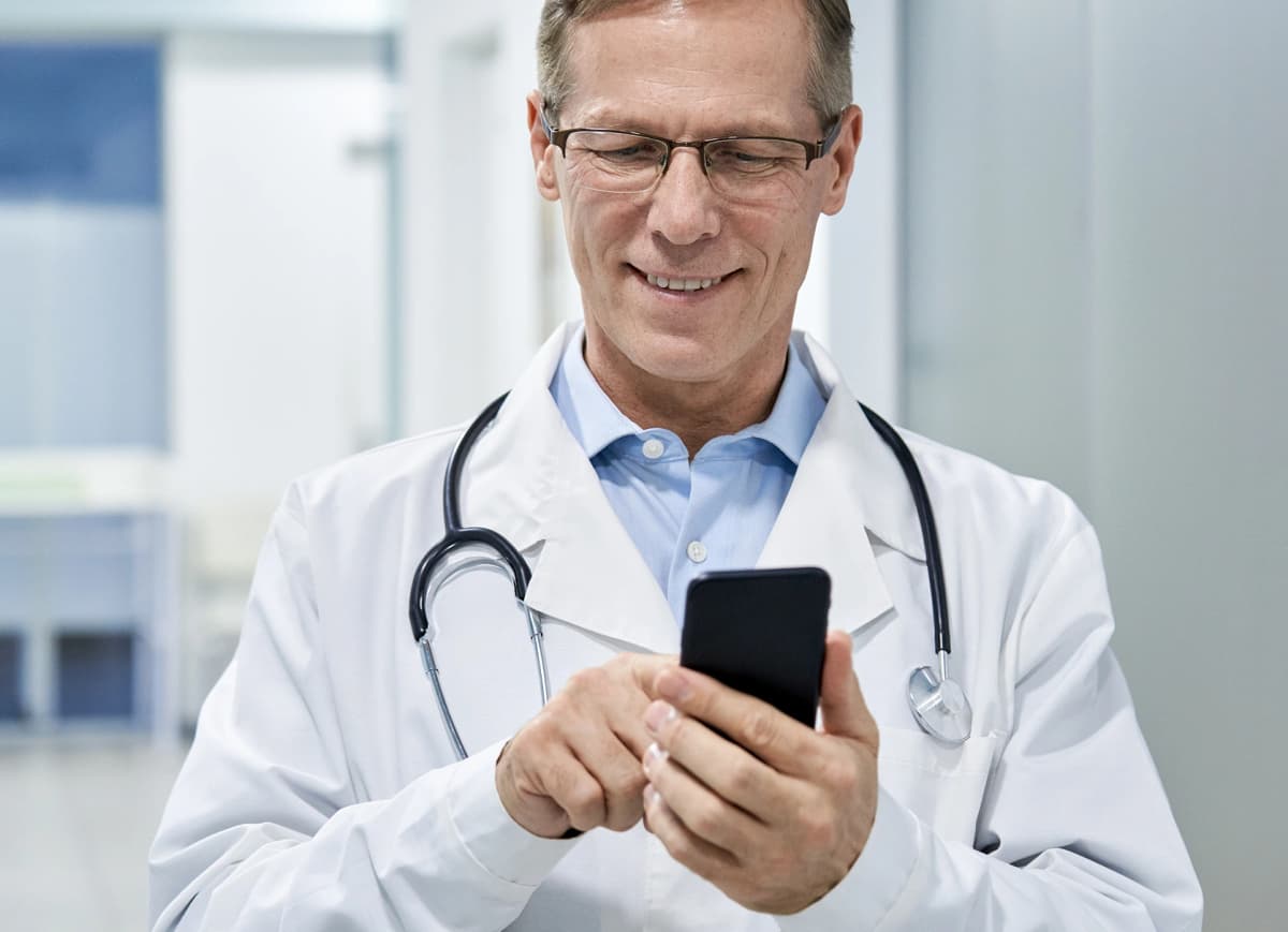 Médico sorrindo enquanto utiliza um smartphone